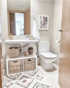 a white bathroom with baskets on the floor and a rug in front of the toilet