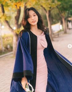 a woman in a blue and black graduation gown holding a flower bouquet while walking down the street