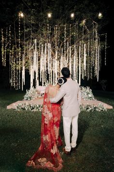 a bride and groom standing in front of a tree with lights hanging from it's branches