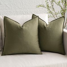 two green pillows sitting on top of a white couch next to a vase with flowers