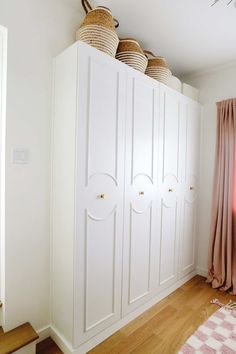 a white closet with baskets on top of it and pink curtains in the window sill