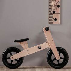 a wooden toy bike sitting on top of a hard wood floor next to a gray wall