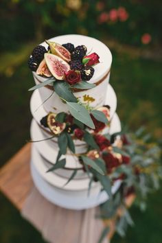 a three tiered cake with fruit and flowers on it's top is decorated with greenery