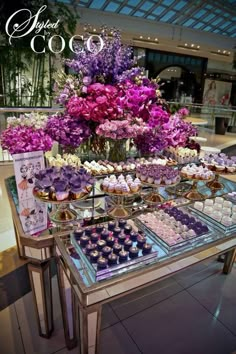 a table filled with cupcakes and purple flowers