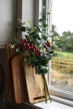 a wooden cutting board sitting next to a window sill filled with berries and greenery