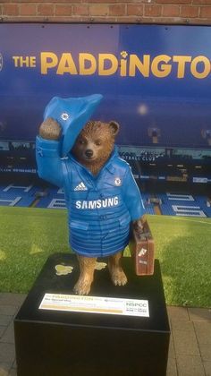 a statue of a teddy bear wearing a blue jacket and holding a soccer ball in his hand