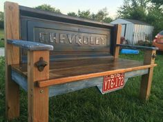 a wooden bench sitting in the grass with a chevrolet sign on it's back