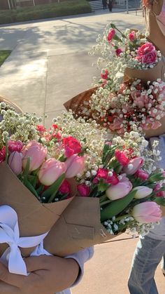 two women holding bouquets of flowers in their hands while standing on the side walk