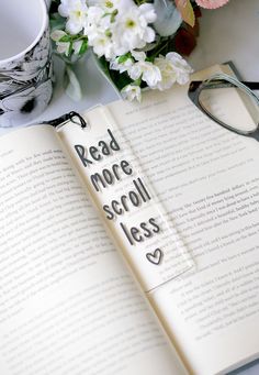 an open book with the words read more scroll less on it next to glasses and flowers