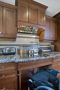 a kitchen with wooden cabinets and granite counter tops, along with a wheelchair parked in front of the sink