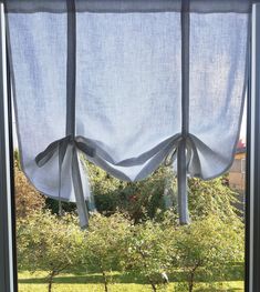 an open window with white curtains hanging from it's sides and trees in the background