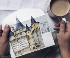 a person holding a cup of coffee next to a paper with a castle on it