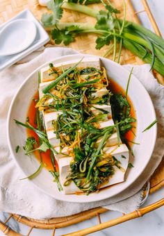 a white plate topped with tofu covered in greens and sauce on top of a table