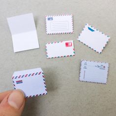 a hand holding a piece of paper next to several envelopes and postcards on a table