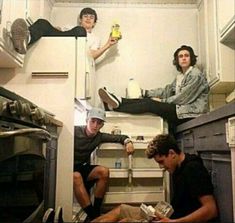 three young men sitting on the floor in a small kitchen, one holding a bottle