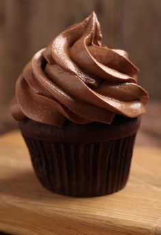 a cupcake with chocolate frosting sitting on top of a wooden cutting board