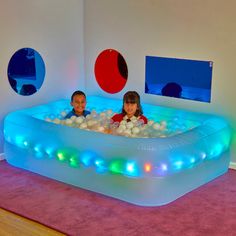 two children are in an inflatable pool with balls on the floor and lights around it