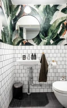 a bathroom with white tile and green leaves painted on the wall above the sink, toilet and mirror