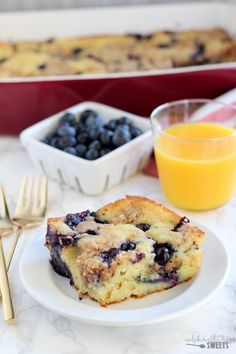 a white plate topped with blueberry coffee cake next to a glass of orange juice