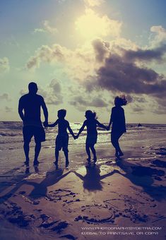 a family holding hands while walking on the beach at sunset with clouds in the background