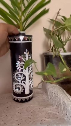 a hand holding a black and white vase next to a potted plant on a table