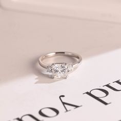 a three stone diamond ring sitting on top of a white book with the word, no 4