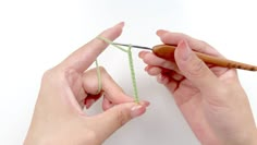 two hands are knitting together with yarn and a crochet hook in front of them