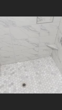 a white shower with hexagonal tiles and a drain in the floor next to it