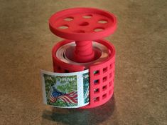 a red object sitting on top of a table next to a roll of paper and a stamp