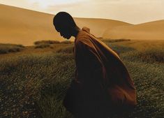 a man standing in the middle of a field next to tall grass and sand dunes