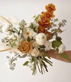 a woman holding a bouquet of flowers in her hand with white, orange and yellow colors