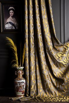 a vase sitting next to a window covered in yellow and grey fabric with an image of a woman behind it