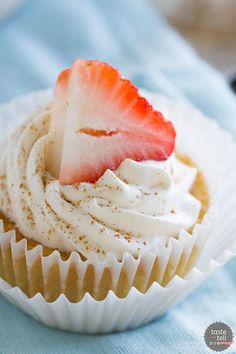 a cupcake with white frosting and a strawberry on top sitting on a blue napkin