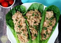 two lettuce wraps filled with meat on top of a white plate next to tomatoes