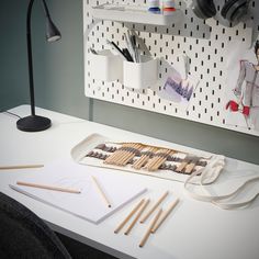 an assortment of crafting supplies on a desk with a lamp and wall hangings