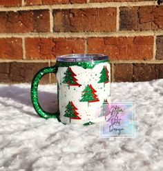 a green and white coffee mug with christmas trees on it sitting in front of a brick wall