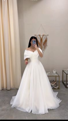 a woman taking a selfie wearing a white wedding dress with off the shoulder sleeves