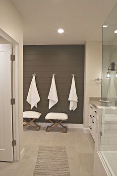 a bathroom with three white towels hanging on the wall and two stools next to it