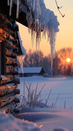 icicles hanging from the roof of a cabin in winter time with sun setting behind it