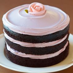 a three layer chocolate cake with pink frosting and a single rose on the top