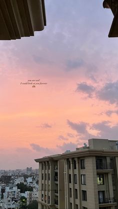 the sky is pink and purple with some buildings in the foreground, and an airplane flying overhead