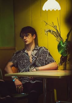 a man sitting at a table with a plant in front of him and a lamp on the wall behind him