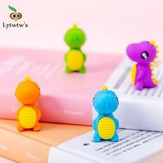 three small toy animals sitting on top of a book next to each other and one is purple, green, yellow