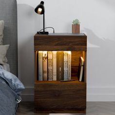 a night stand with books on it next to a bed