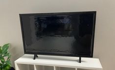 a flat screen tv sitting on top of a white shelf next to a potted plant