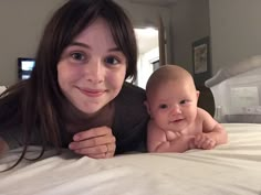 a woman laying on top of a bed with a baby in her lap and smiling at the camera