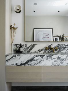 a bathroom vanity with marble counter top and gold faucet, framed art on the wall