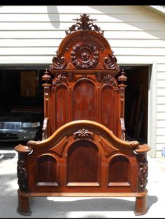 an old wooden bed frame with carvings on the headboard and foot board, in front of a garage