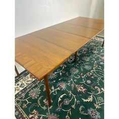 a large wooden table sitting on top of a green rug next to a white wall