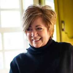 a smiling woman in a black turtle neck sweater holding a plate of food and looking at the camera